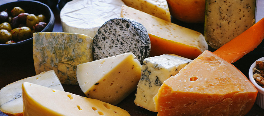 Variety of cheeses; cheddar, brie, etc. Bowl of olives beside.